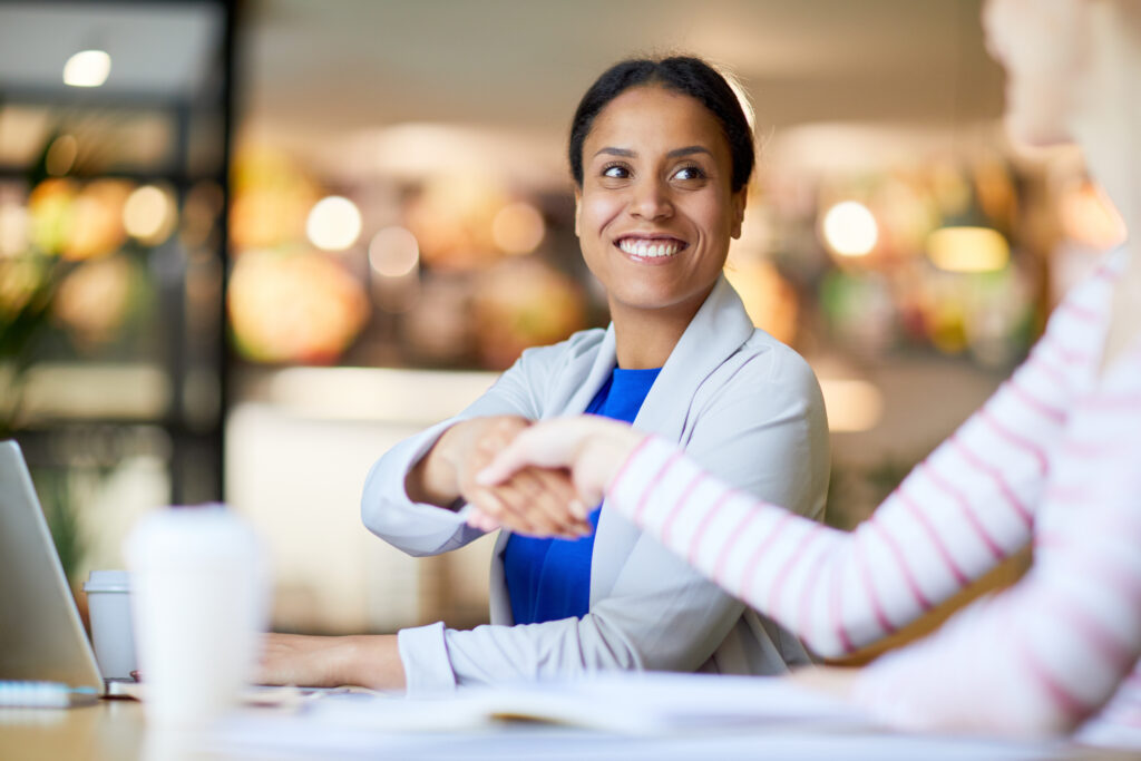 Zakelijke vrouw schudt glimlachend de hand van een collega in een informele werkomgeving.