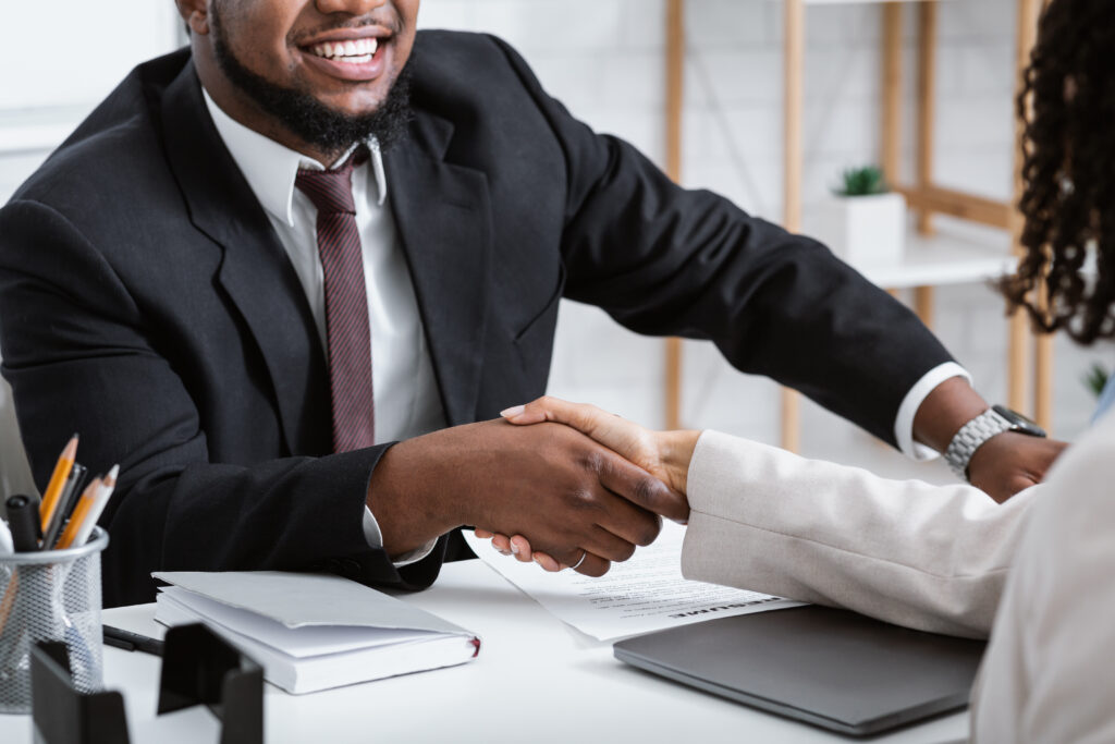 Afrikaanse man in een formeel pak schudt de hand van een collega aan een bureau tijdens een zakelijke afspraak.