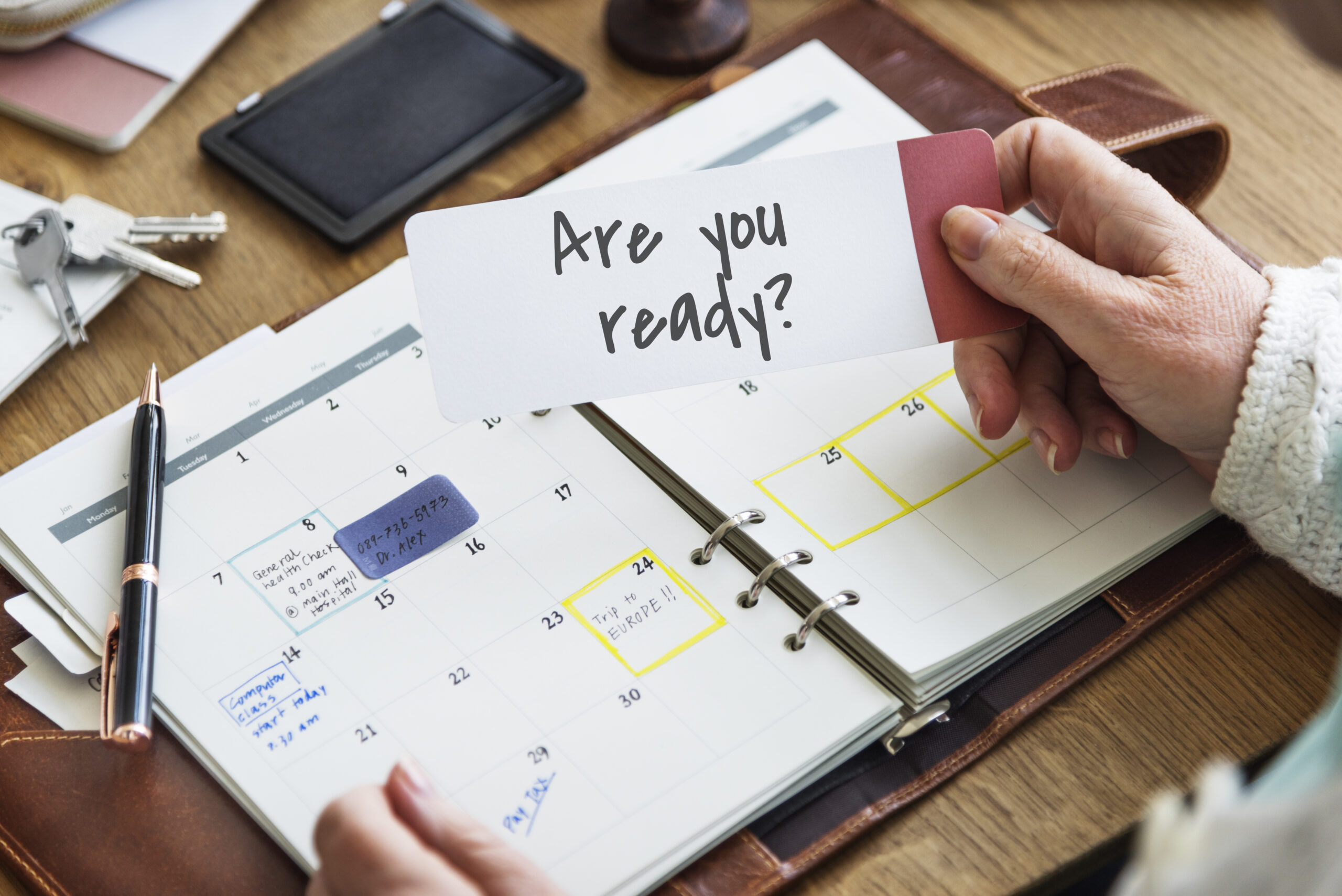 Hand houdt een kaartje vast met de tekst 'Are you ready?' boven een agenda, symbool voor voorbereidheid en planning bij detachering.