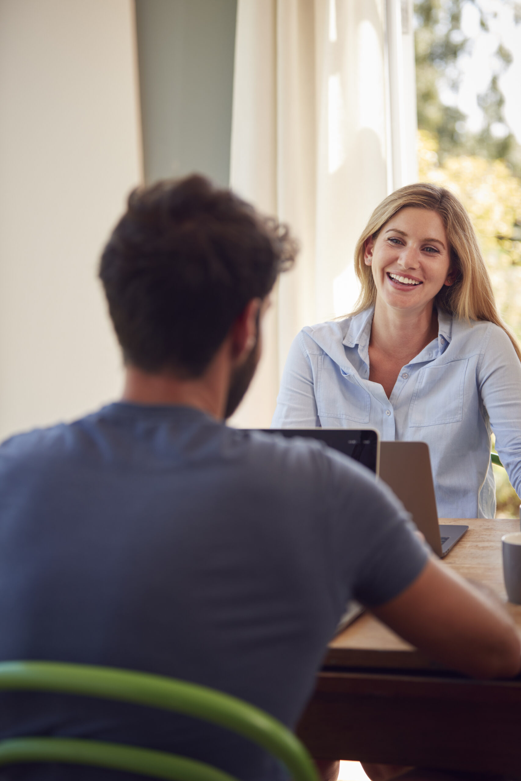 Een jonge vrouw en man in gesprek terwijl ze aan tafel werken, symbool voor het vinden van een vaste baan.