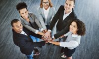 Team van diverse professionals met handen op elkaar, symbool voor samenwerking en inclusiviteit